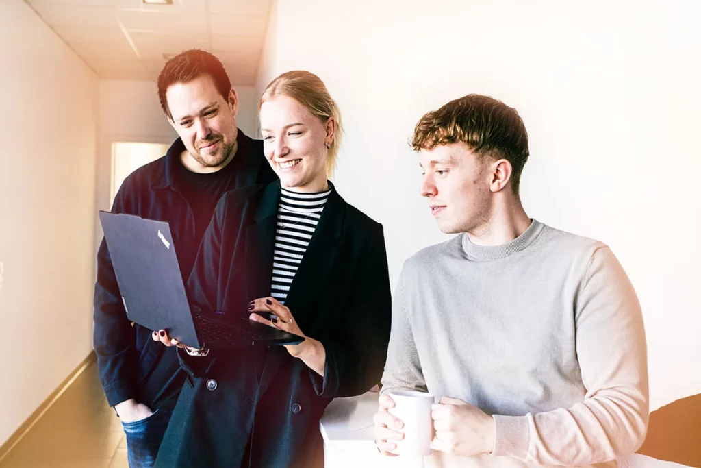 Drei Personen stehen im Büroflur und schauen gemeinsam auf einen geöffneten Laptop